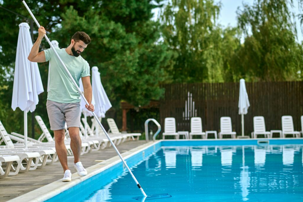 Hombre haciendo la limpieza de la piscina con una red guía de mantenimiento básico de una piscina